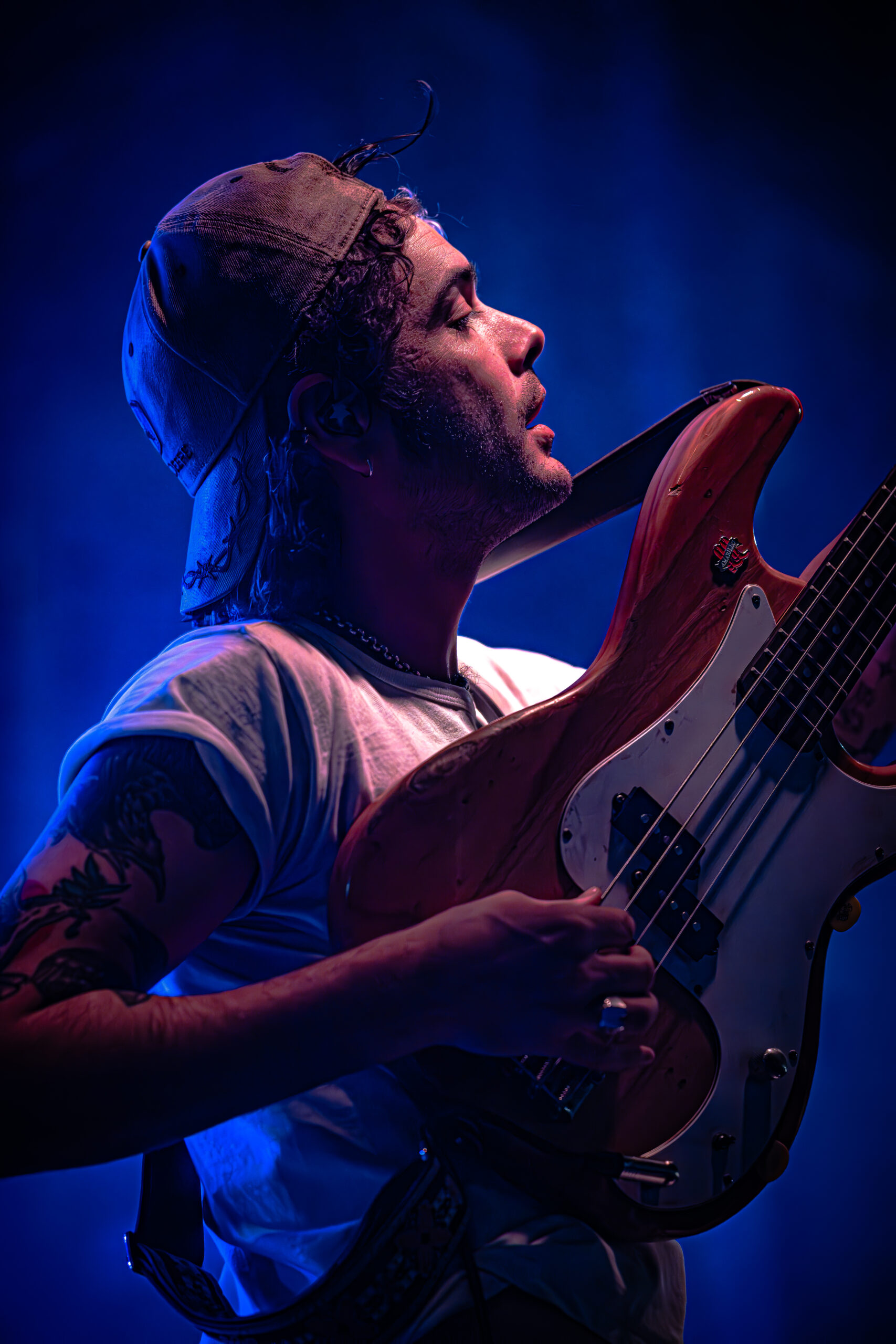 Musician intently playing the bass guitar on stage under blue lighting.