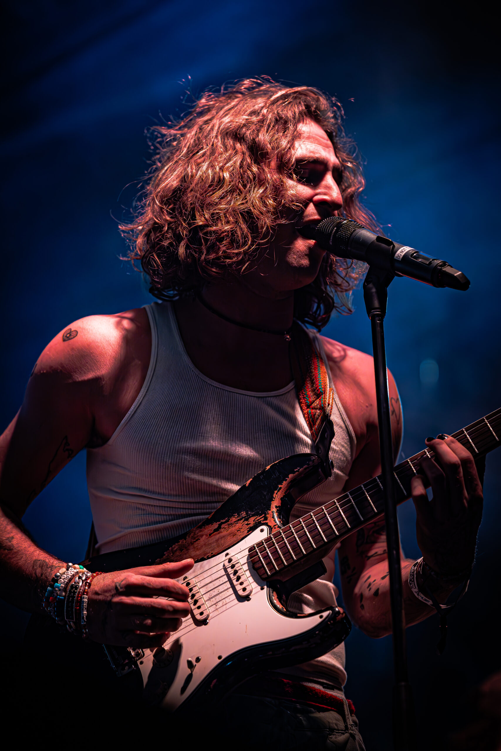 Musician singing and playing guitar on stage with intense emotion.