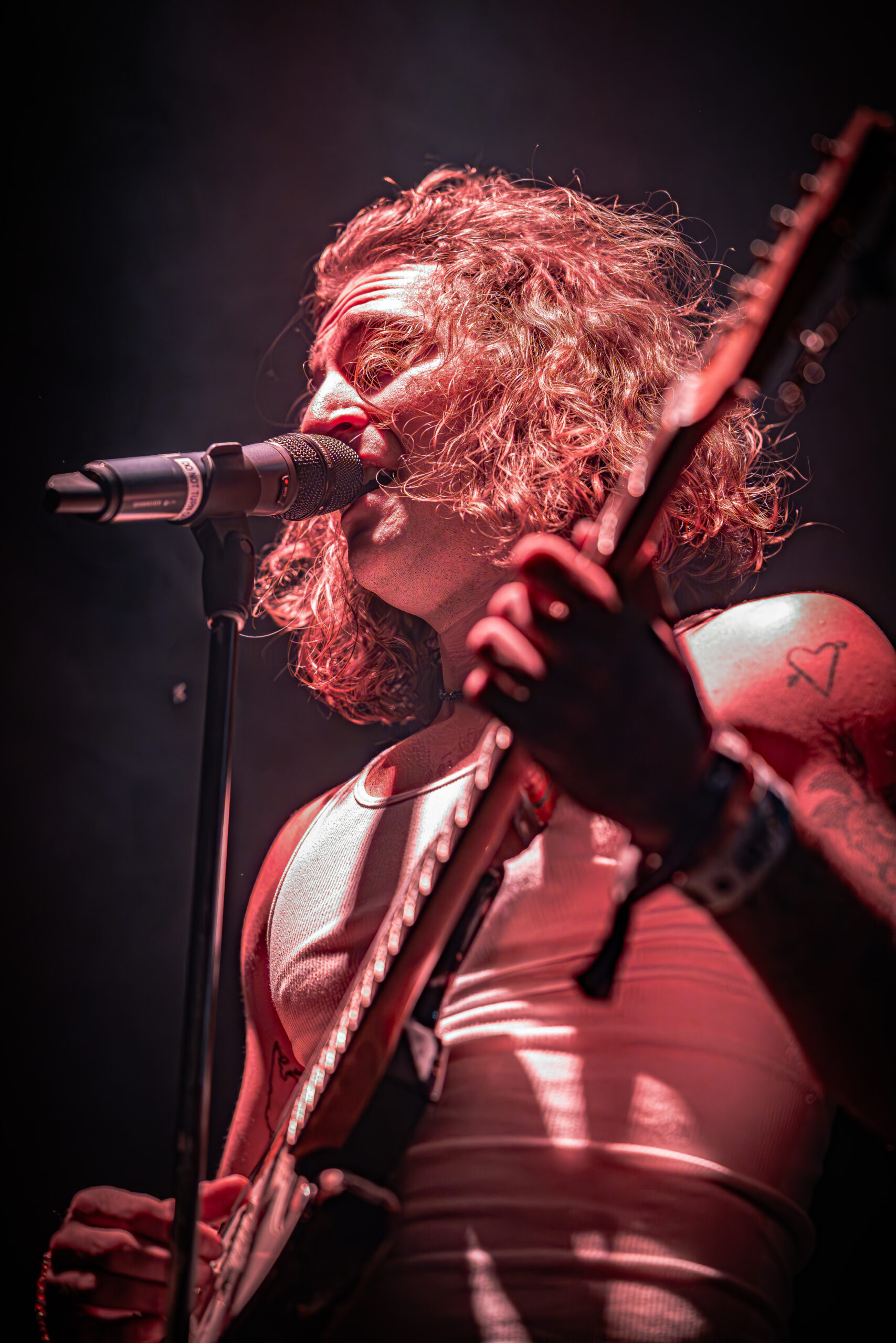 Musician singing and playing guitar on stage with intense emotion.