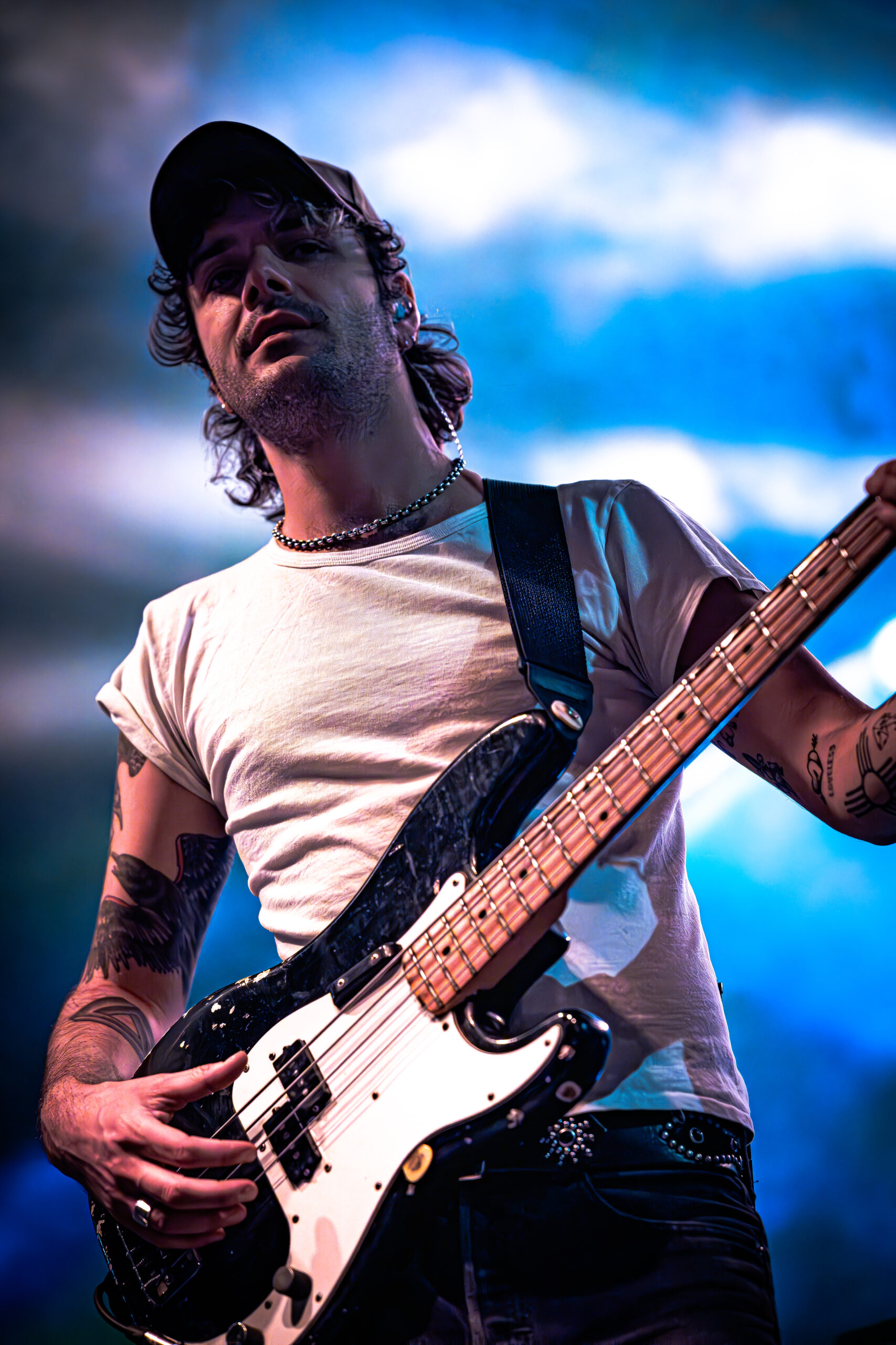 Bass guitarist in focused performance under blue sky-like lighting.