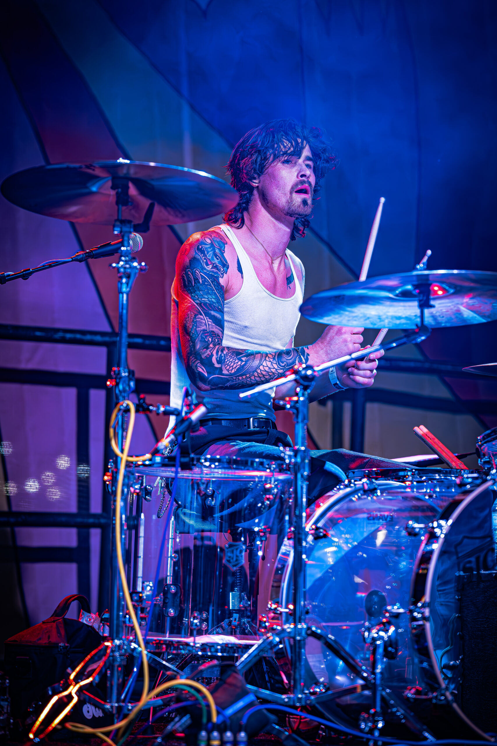 Focused drummer playing at a concert with vibrant stage lighting.