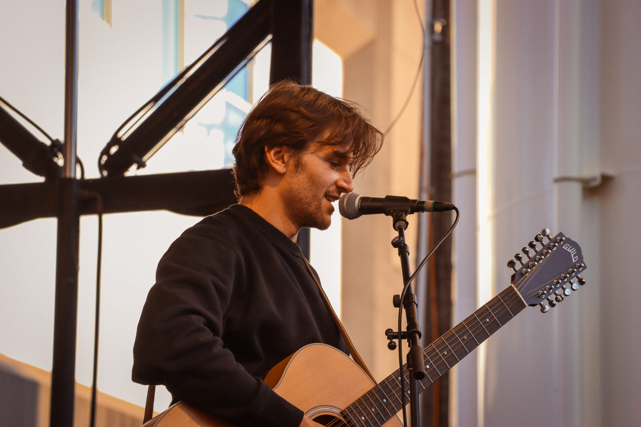 Jonah Kagen performing live at Treefort Music Festival 2024, singing into a microphone with a guitar in hand, spotlight illuminating his expressive face.