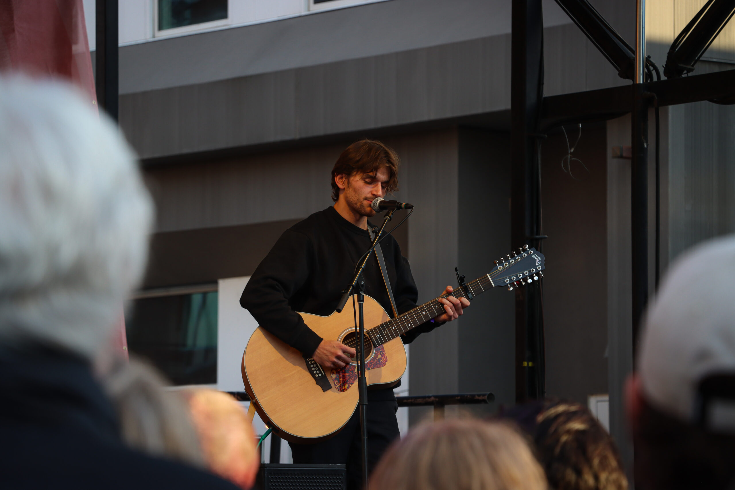 Jonah Kagen performing live at Treefort Music Festival 2024, singing into a microphone with a guitar in hand, spotlight illuminating his expressive face.