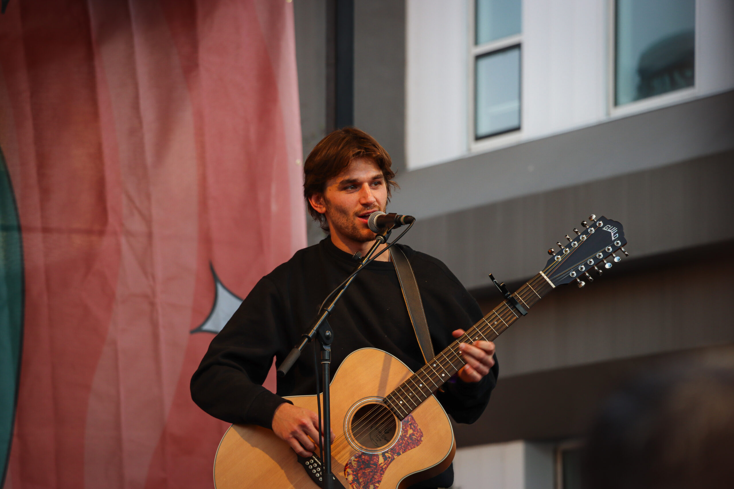 Jonah Kagen performing live at Treefort Music Festival 2024, singing into a microphone with a guitar in hand, spotlight illuminating his expressive face.