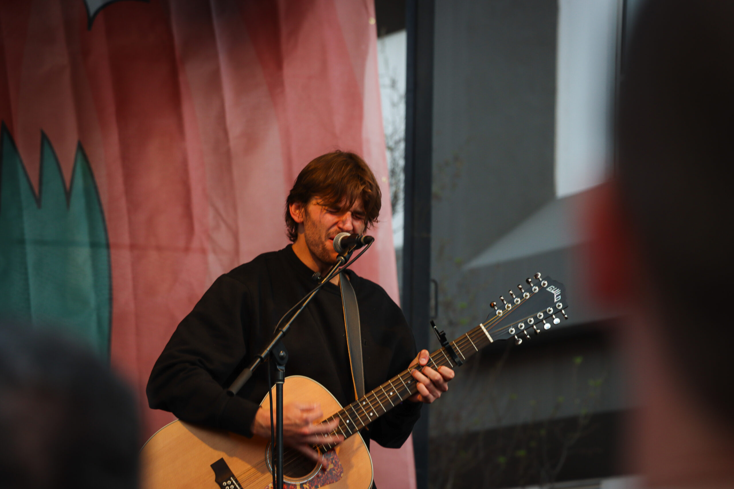 Jonah Kagen performing live at Treefort Music Festival 2024, singing into a microphone with a guitar in hand, spotlight illuminating his expressive face.