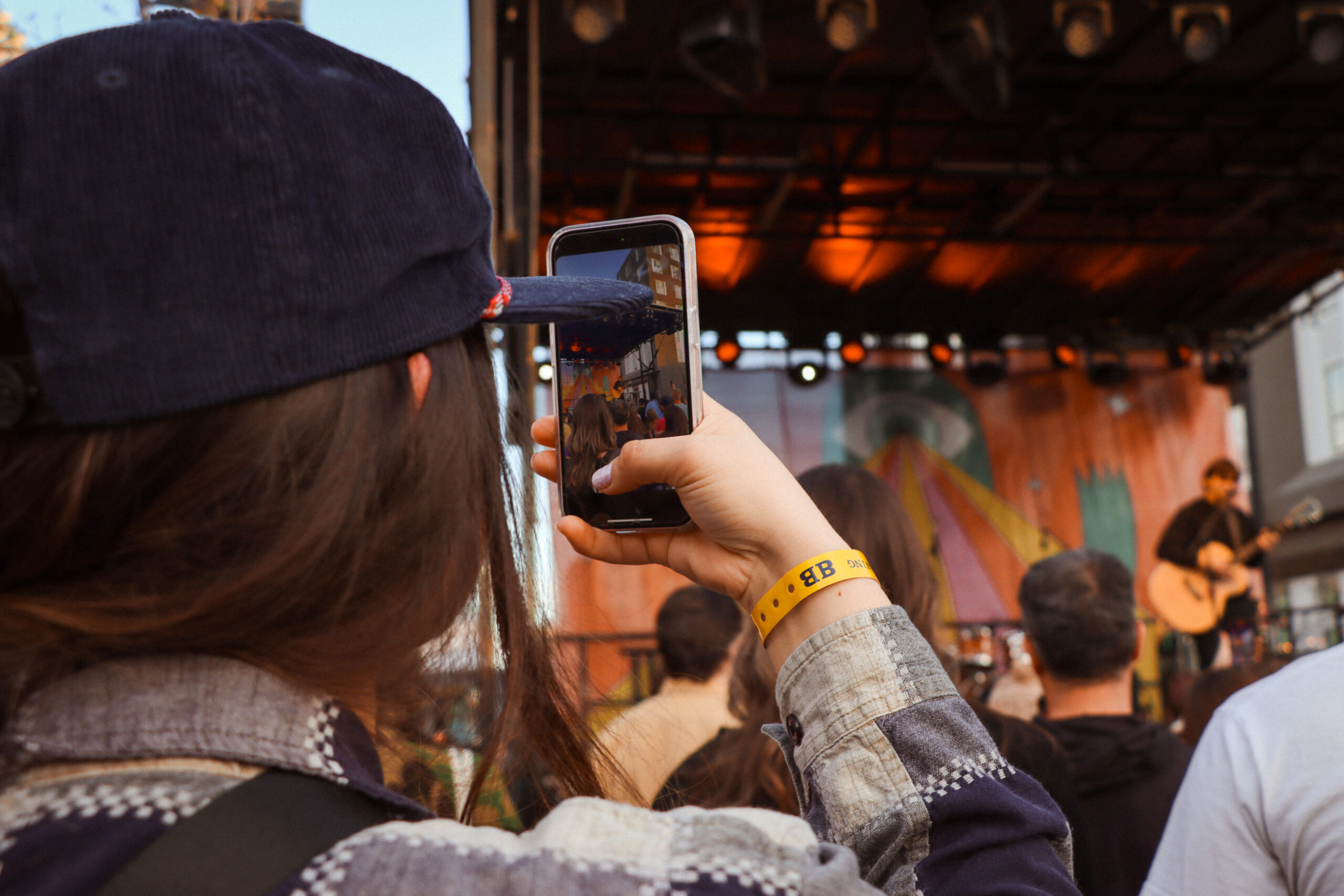 Jonah Kagen performing live at Treefort Music Festival 2024, singing into a microphone with a guitar in hand, spotlight illuminating his expressive face through the lens of an fans camera.