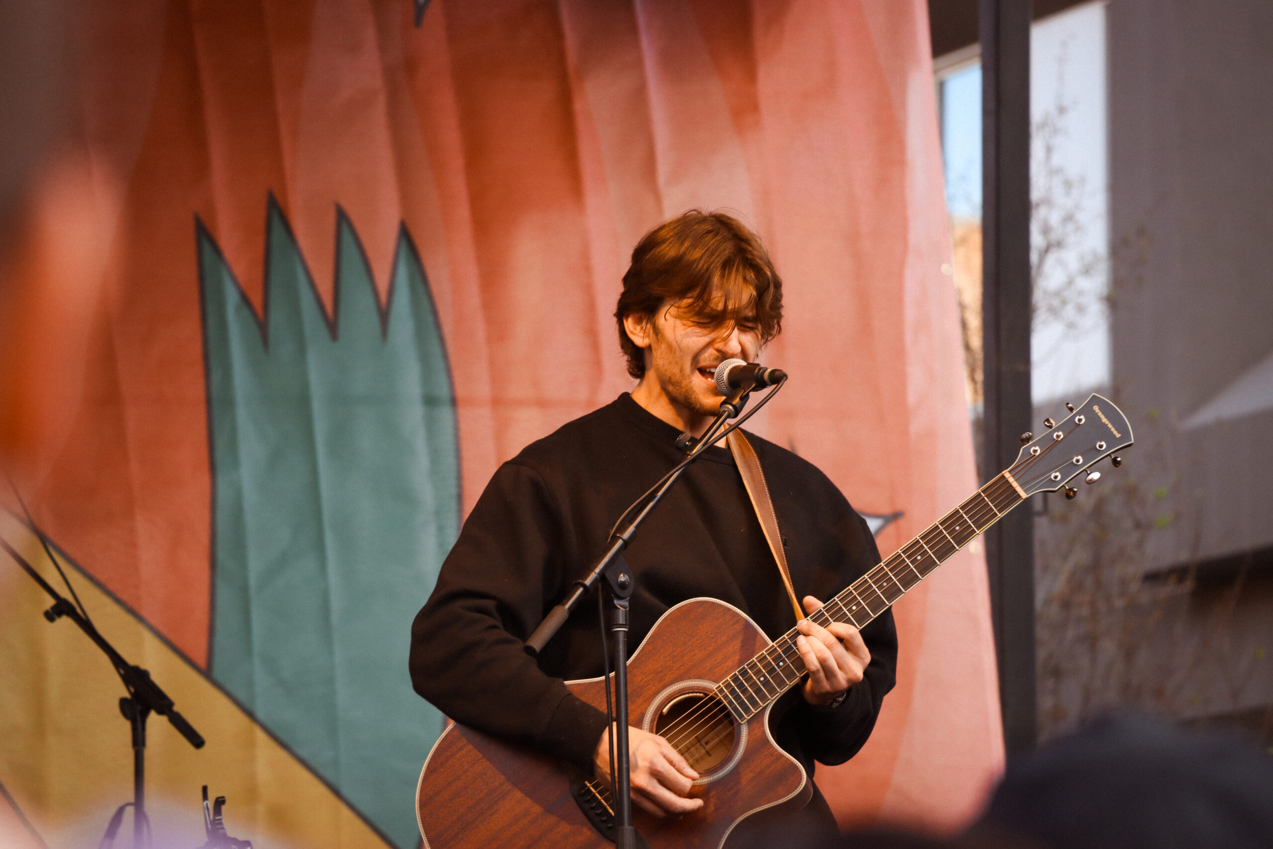 Jonah Kagen performing live at Treefort Music Festival 2024, singing into a microphone with a guitar in hand, spotlight illuminating his expressive face.