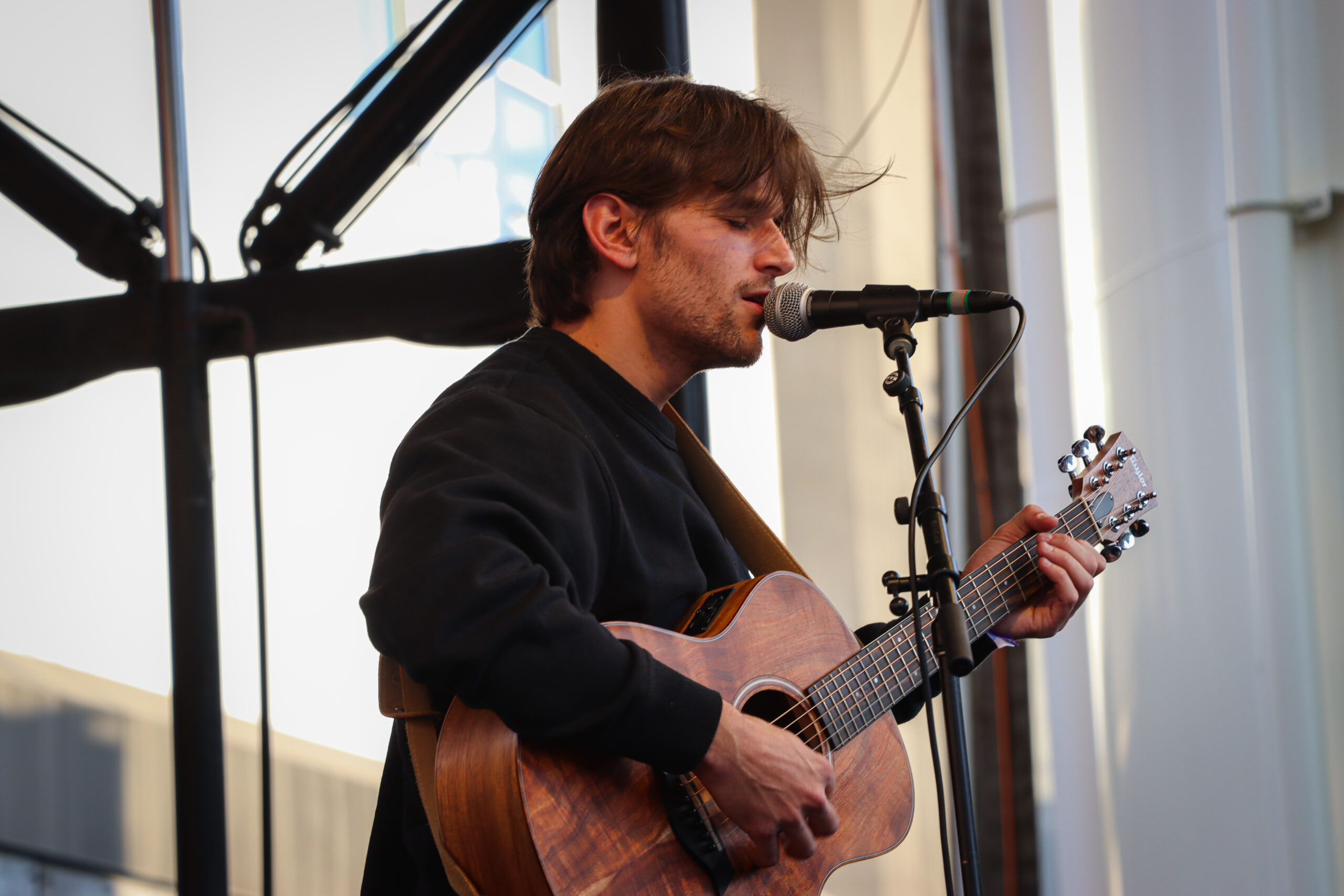 Jonah Kagen performing live at Treefort Music Festival 2024, singing into a microphone with a guitar in hand, spotlight illuminating his expressive face.