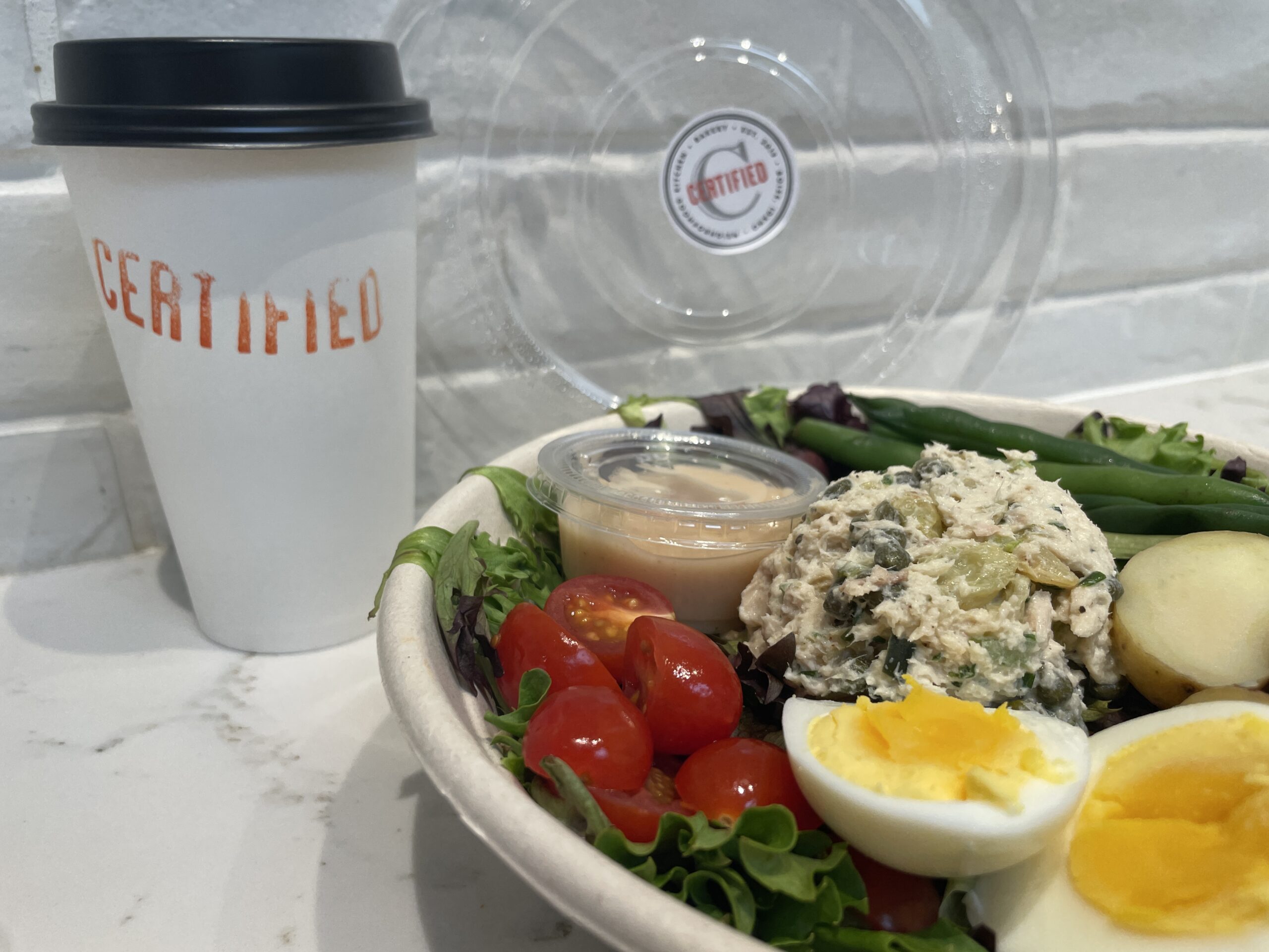 A frothy Havana Latte with caramel drizzle on top, served in a tall glass at Certified Bakery. Fresh Tuna Nicoise salad with mixed greens, olives, roasted potatoes, tomatoes, and green beans, dressed in garlic vinaigrette at Certified Bakery.