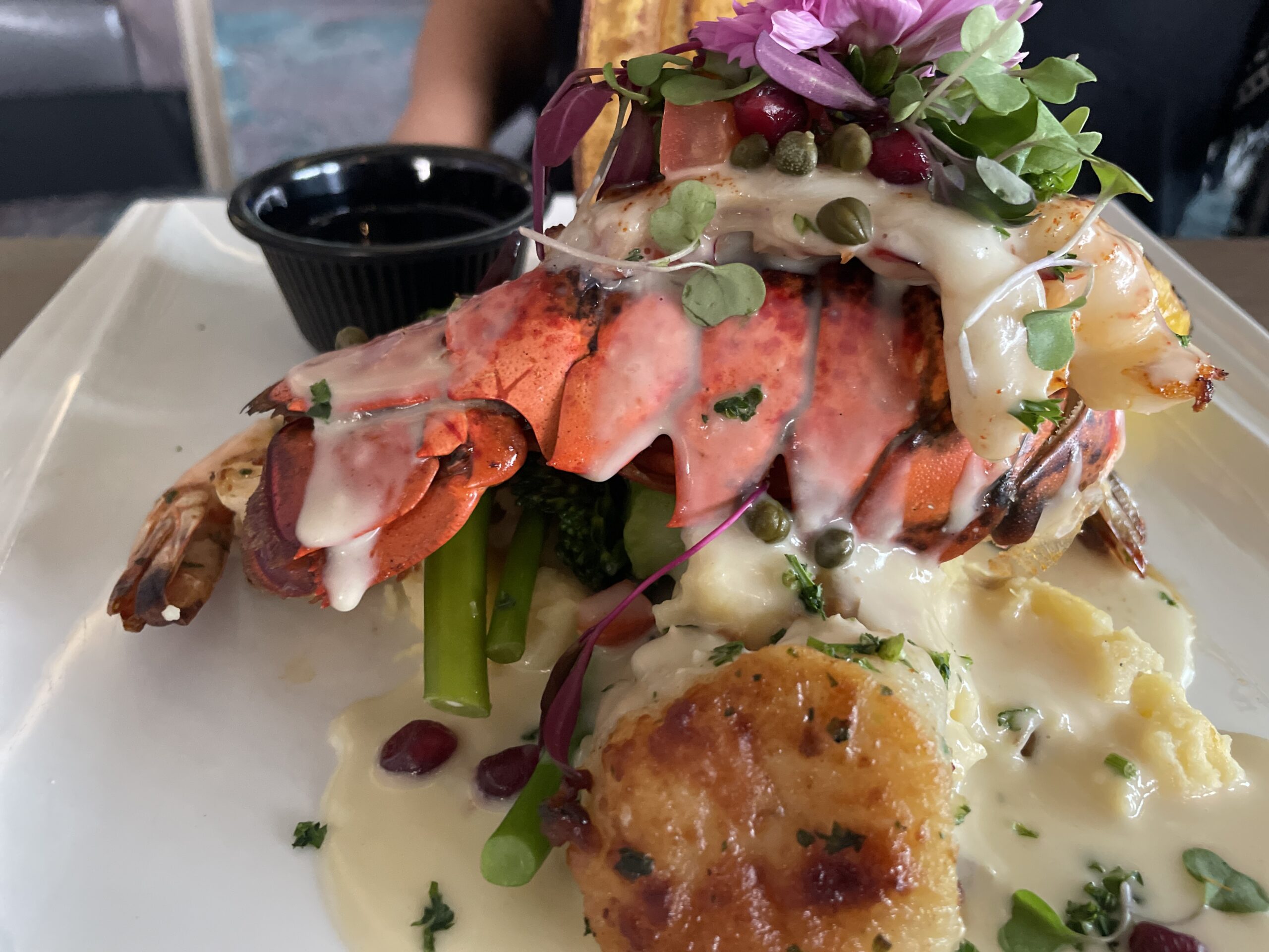 Coa Del Mar Grilled Seafood Platter featuring Lobster tail, jumbo shrimp, scallops, mashed potatoes & broccolini. Served with a pomegranate lemon-caper beurre blanc