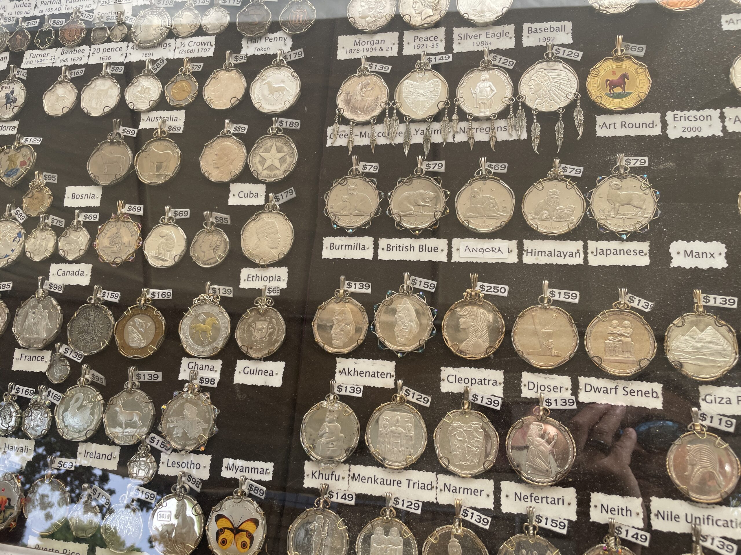 Display of intricately designed coin pendants from different countries, including Ethiopia, Ghana, and France, at Art in the Park Boise 2024.