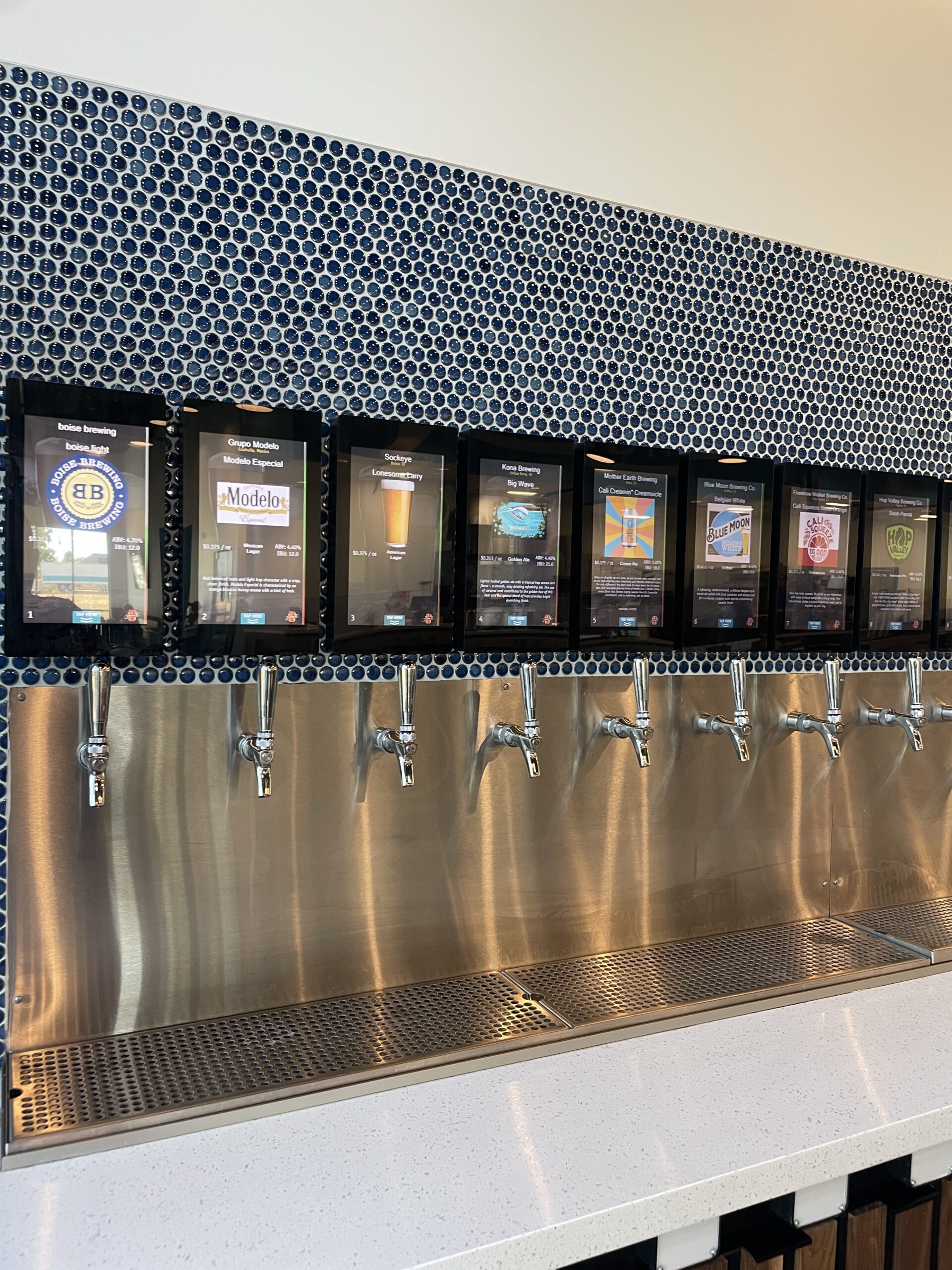 Modern beer tap wall at Longboards Pizza in Nampa, Idaho, featuring a variety of craft beers on tap with digital displays showing beer details.