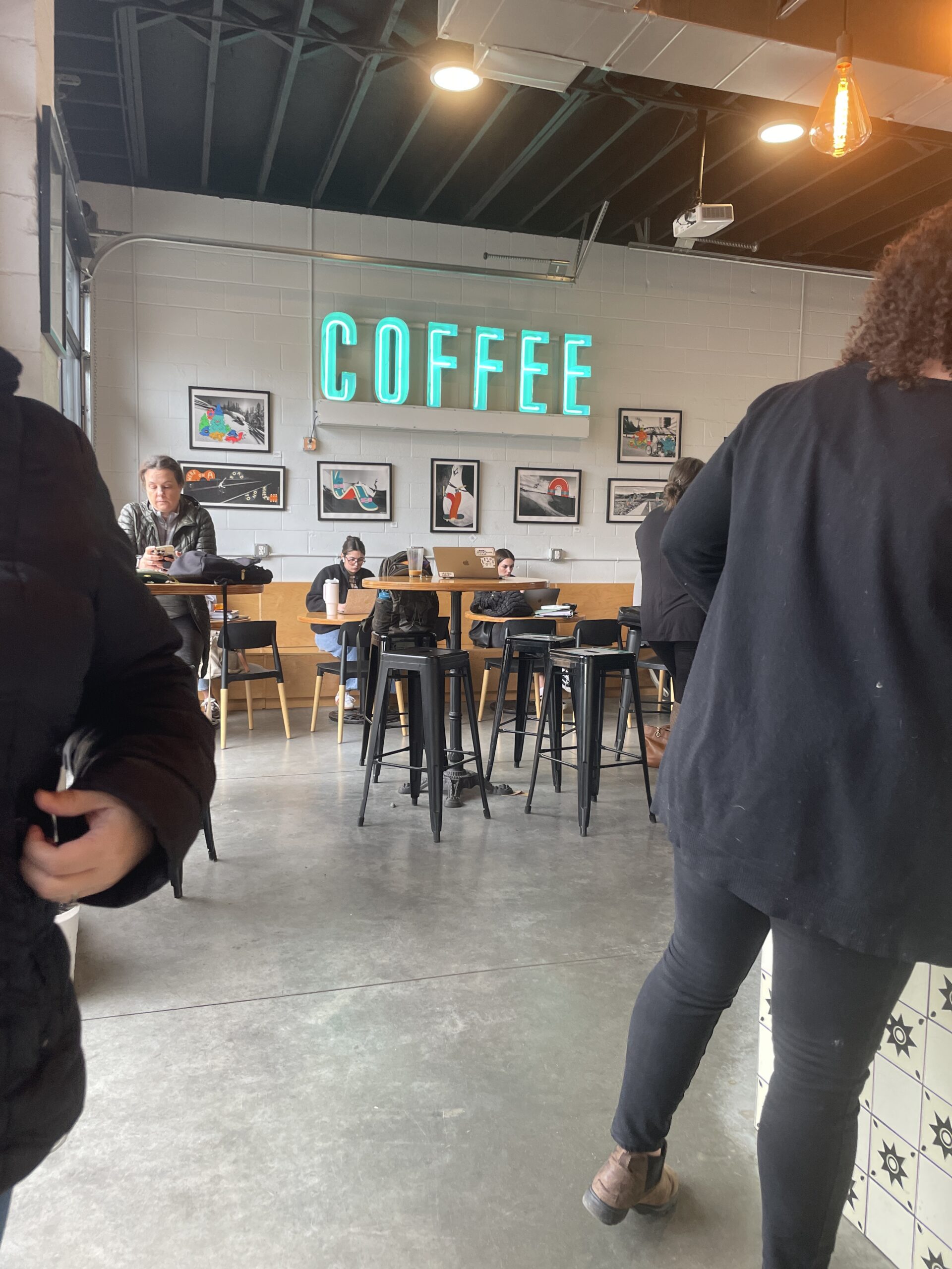 The seating area of a modern coffee shop with a glowing "COFFEE" sign and patrons enjoying their drinks.