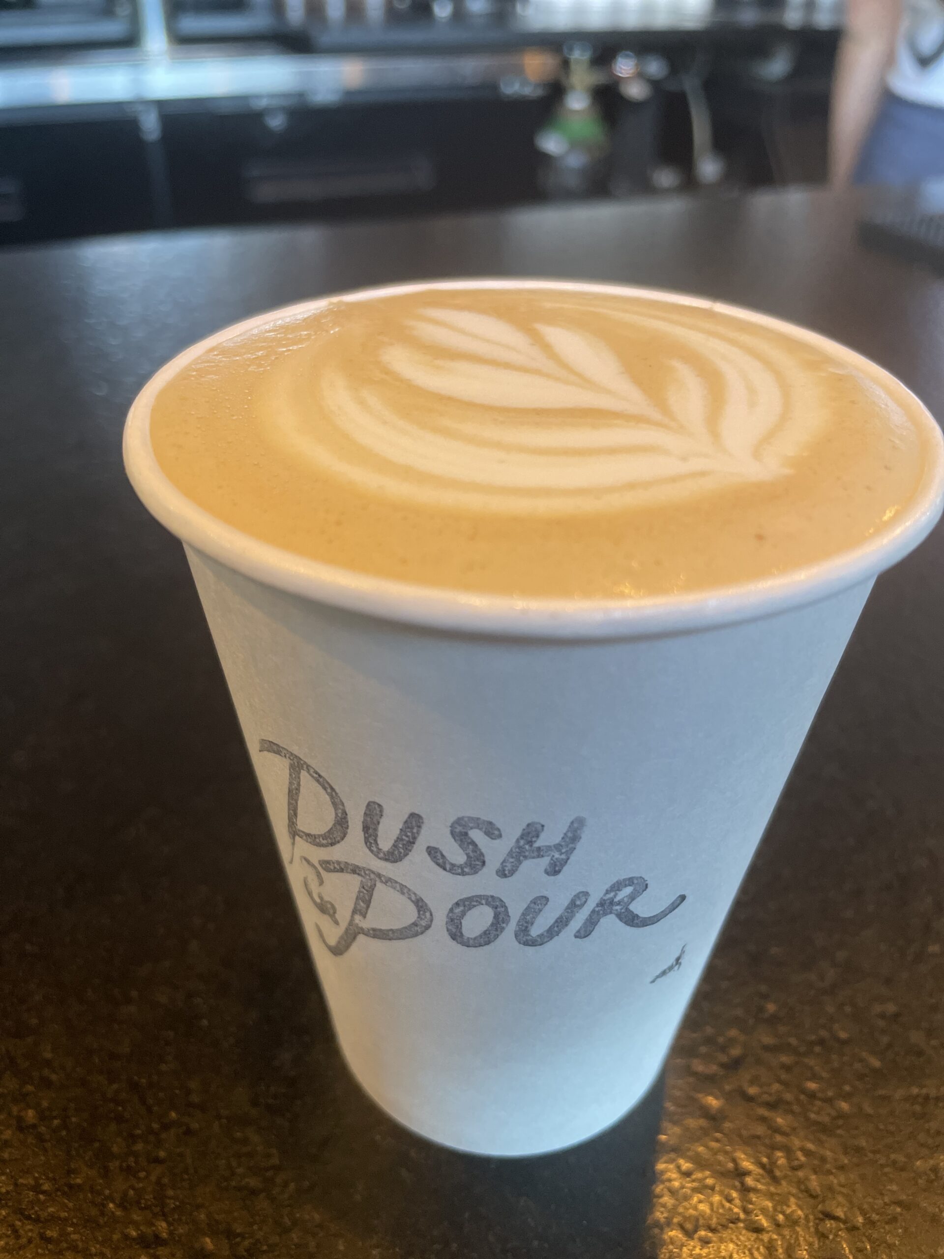 A cup of latte with beautiful latte art served in a Push and Pour branded cup.