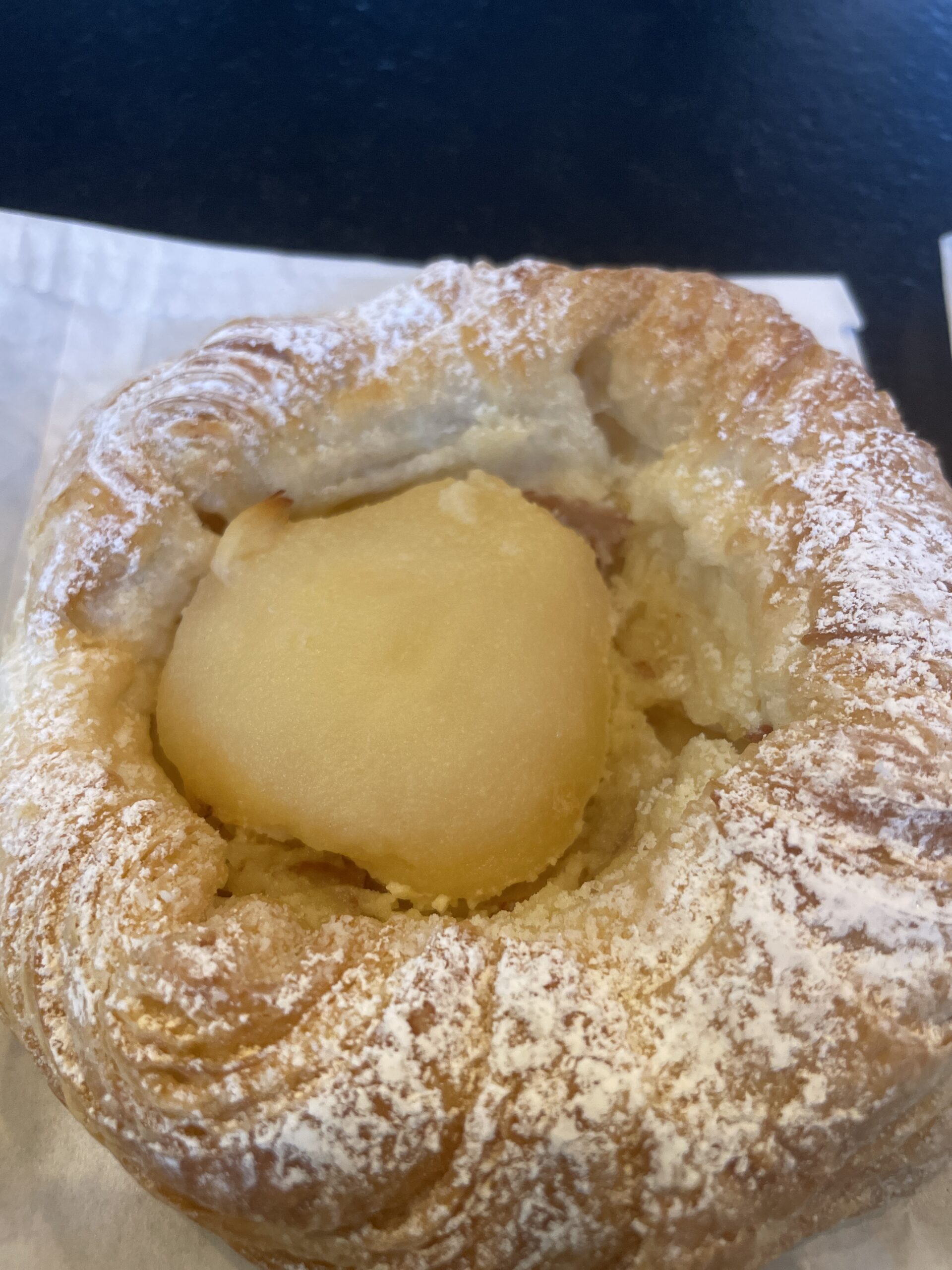 A golden, flaky pear croissant dusted with powdered sugar.