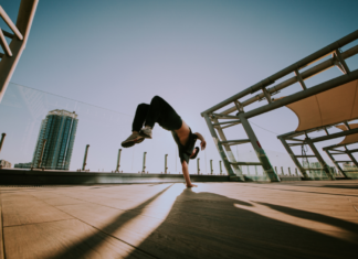 Breakdancer performing a handstand flip on an outdoor rooftop with a cityscape in the background.