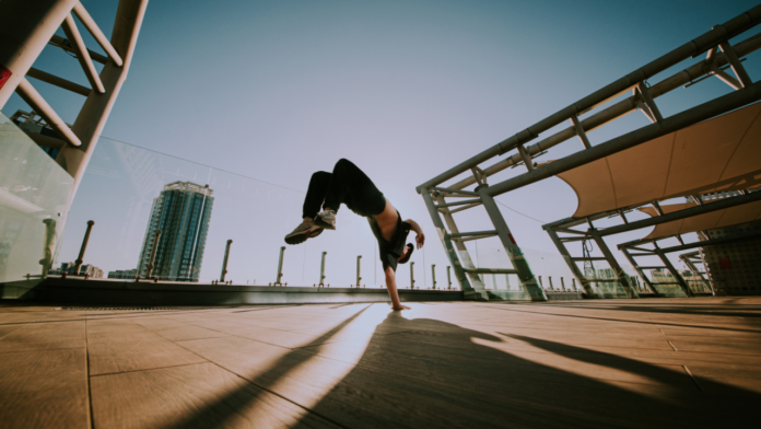 Breakdancer performing a handstand flip on an outdoor rooftop with a cityscape in the background.