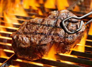 Juicy grilled steak cooking over an open flame on a barbecue grill.