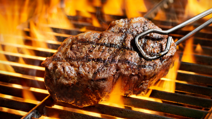 Juicy grilled steak cooking over an open flame on a barbecue grill.