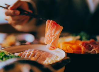 A person dipping thinly sliced beef into a steaming hot pot filled with fresh vegetables and broth at a Japanese shabu shabu restaurant.