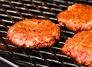 Seasoned raw beef patties cooking on a hot grill.