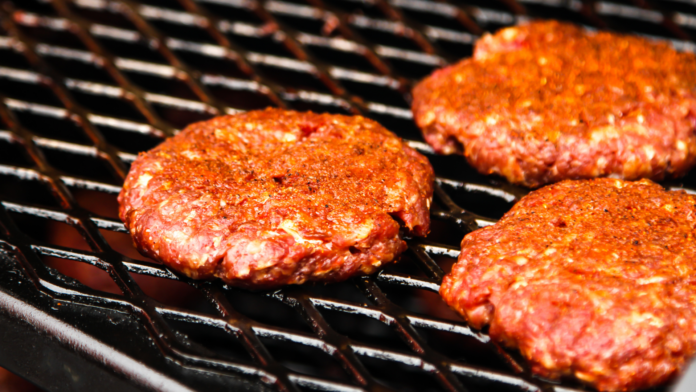 Seasoned raw beef patties cooking on a hot grill.