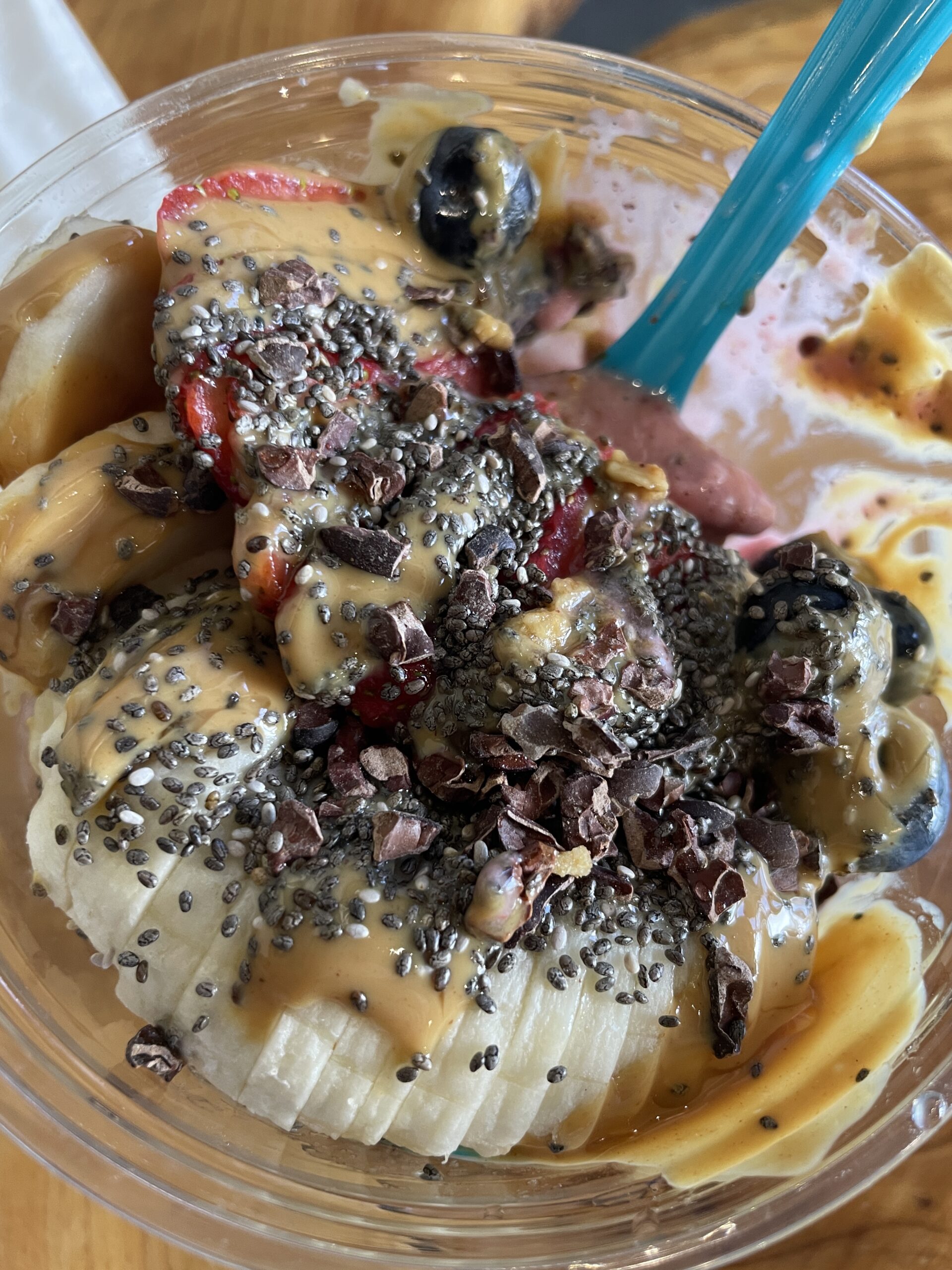 A close-up of Nekter Juice Bar's Peanut Butter Bowl, featuring banana slices, strawberries, blueberries, cacao nibs, chia seeds, and peanut butter drizzle.