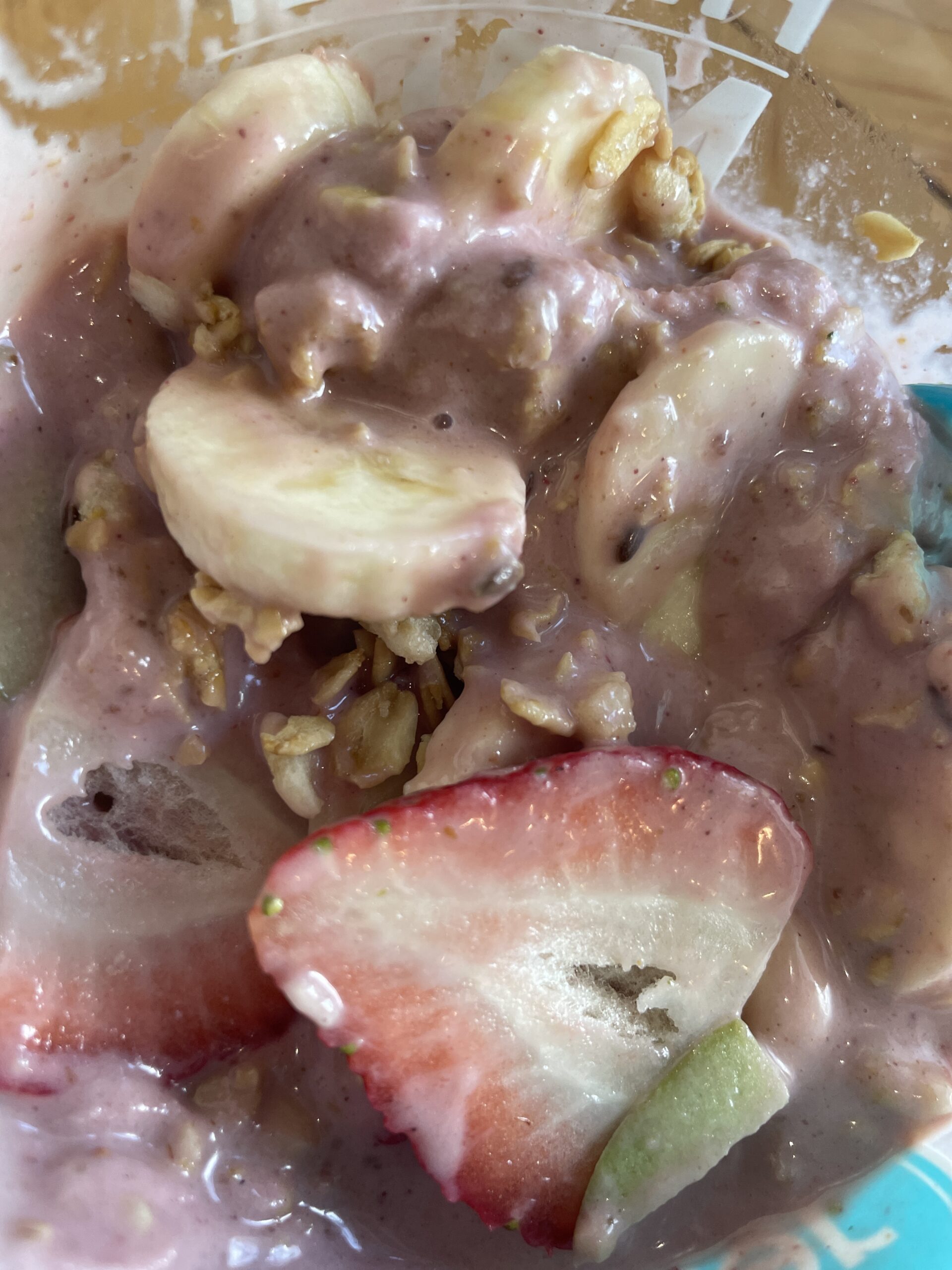 A partially eaten acai bowl from Nekter Juice Bar, showing banana slices, strawberries, granola, and a creamy acai blend.