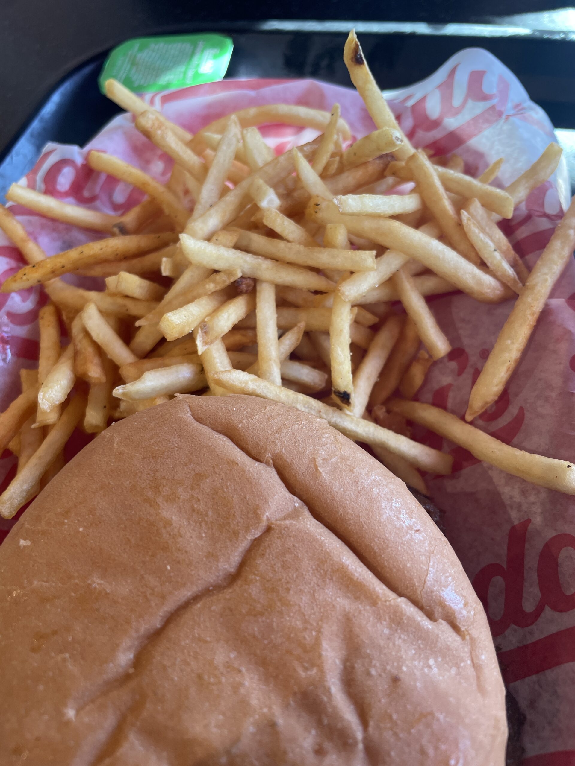 A Freddy’s steakburger with thin, crispy fries served on branded paper.