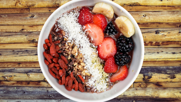 Nekter Juice Bar A vibrant acai bowl topped with goji berries, cacao nibs, shredded coconut, blackberries, bananas, and strawberries on a rustic wooden table.