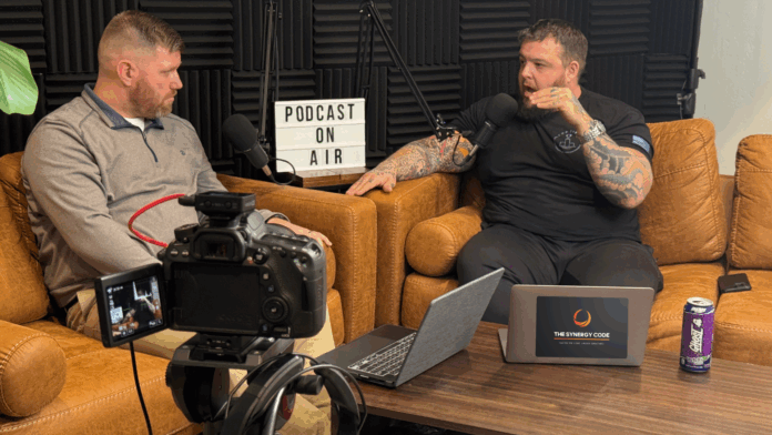 Synergy Code - EP 4 Two men recording Episode 4 of The Synergy Code podcast in a professional studio setting, with microphones, laptops, and a camera setup.