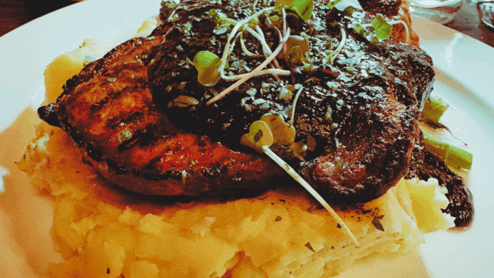 Corso Italian Steak Snake River Farms porkchop served at Corso Italian Steakhouse in Boise, Idaho; topped with bourbon bacon jus and microgreens over creamy mashed potatoes.