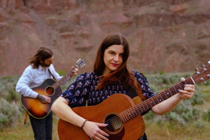 CactusMoon_Day4Night_1-scaled Chelsea Smith and Freeman DeJongh of Cactus Moon playing acoustic guitars in a desert canyon landscape.