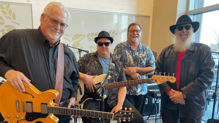 Jeff Engelbert with his band, holding guitars and posing indoors before a blues performance.