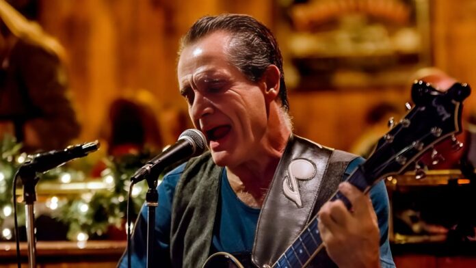 Jersey Johnny 1 A passionate blues guitarist and singer performing live on stage with a microphone and electric guitar, set against warm ambient lighting and festive décor.