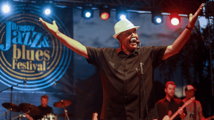 Johnny Rawls Johnny Rawls performing live on stage at a jazz and blues festival, arms raised wide while singing into the microphone.
