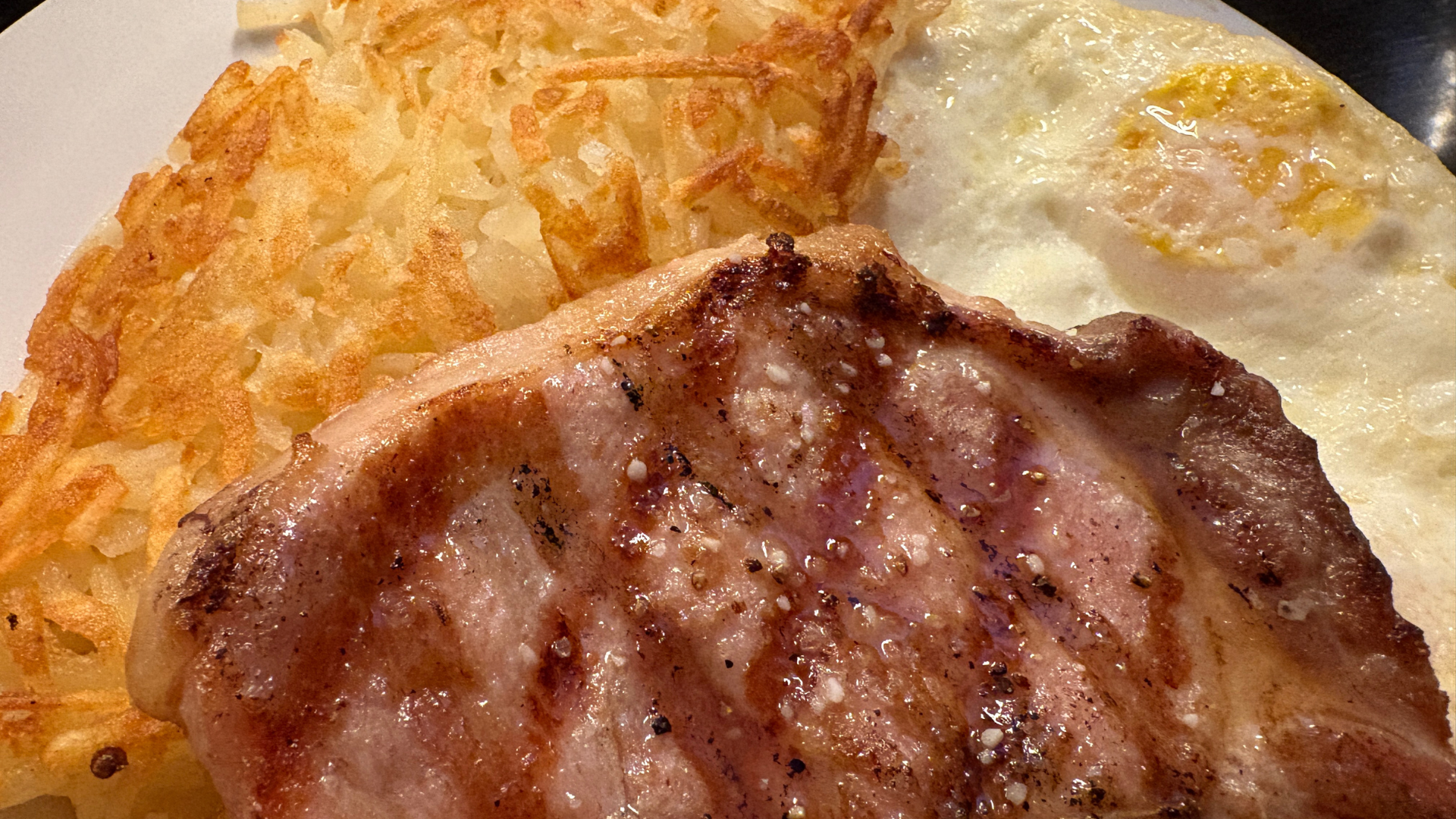Grilled pork chop breakfast with sunny-side egg and crispy hash browns at Rare Steakhouse in Star, Idaho.
