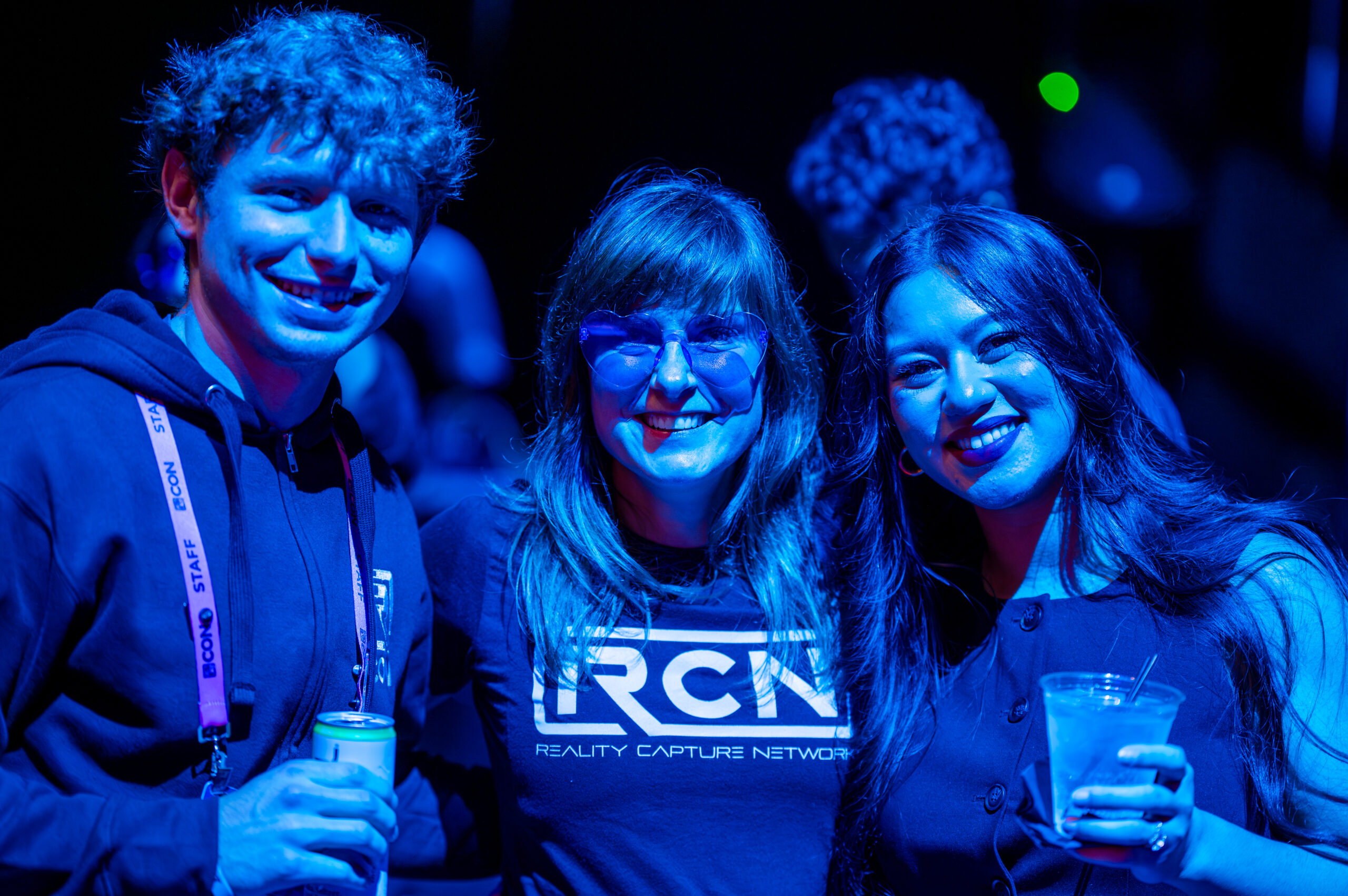 R-CON 2025 attendees smiling at an evening networking event under blue lighting, featuring Reality Capture Network staff enjoying the conference atmosphere.