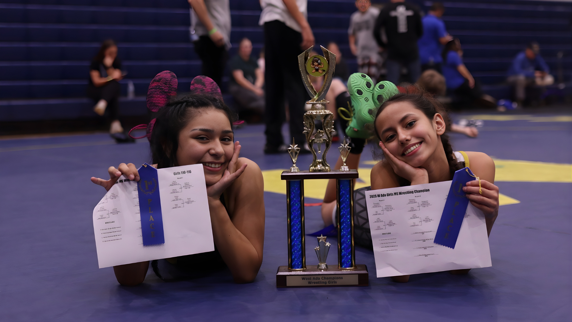 Two Meridian Middle School girls wrestling champions pose with first-place ribbons and trophy at the 2025 West Ada Girls District Championship.
