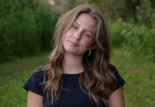 Inside the Creative Mind of Idaho’s Emerging Indie Artist Sydney Dale Close-up portrait of singer-songwriter Sydney Dale outdoors, with loose wavy hair, a black top, and a soft natural expression against a green, blurred forest background.