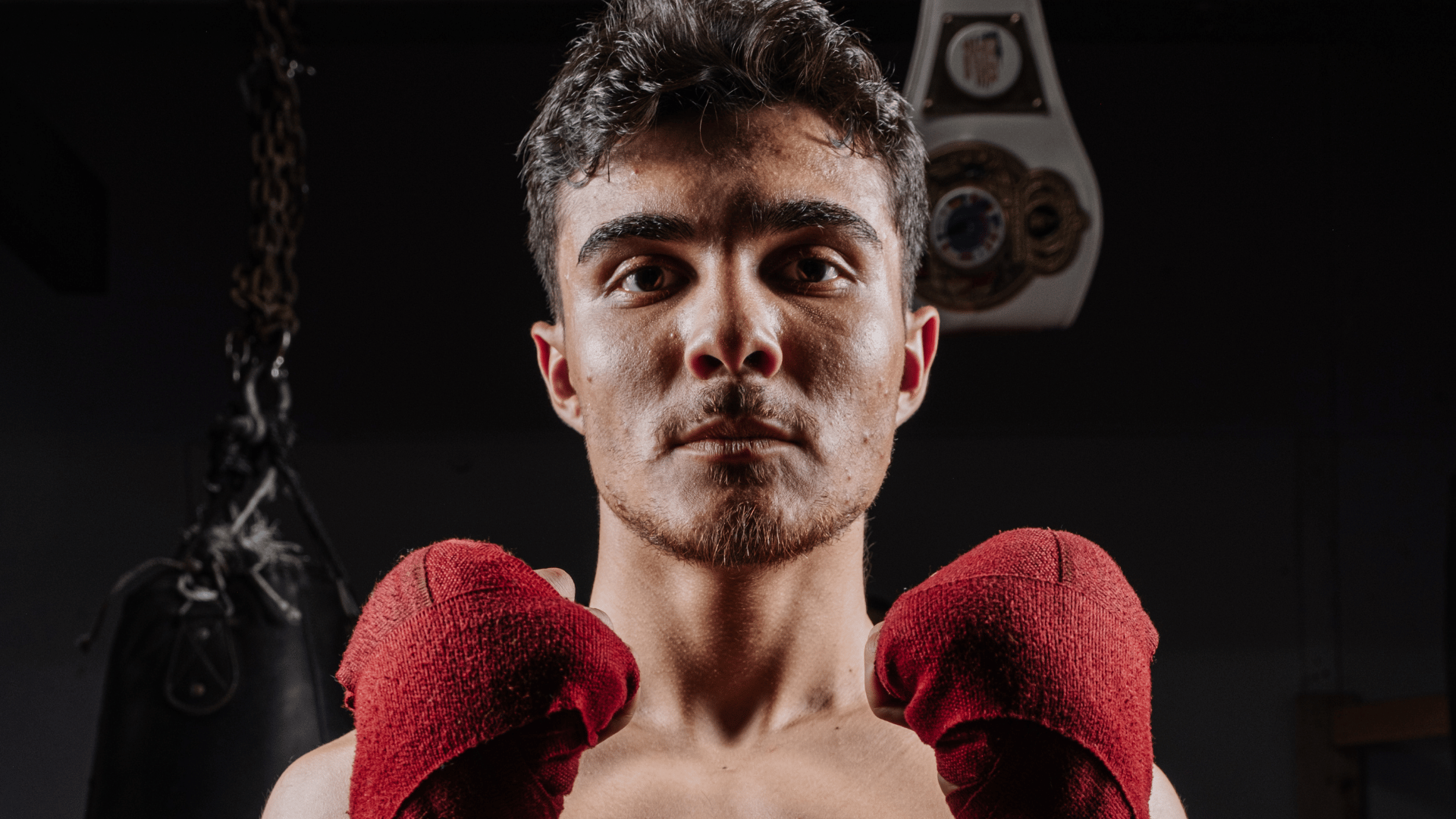 Elias Rivas, an amateur boxer and USA Boxing prospect, poses with red hand wraps in a boxing gym ahead of his national boxing tournament appearance.